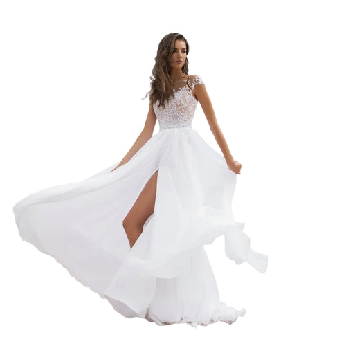 Woman in a white wedding dress with a high slit standing on a beach.