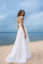Woman in a white dress standing on a beach with a blue sky and ocean in the background