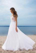 Woman in a white wedding dress standing on a beach with ocean in the background