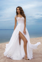 Woman in a white and pink wedding dress standing on a beach with blue sky and water in the background.