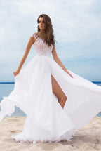 Woman in a white wedding dress with a high slit standing on a beach.