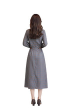 Woman wearing a gray plaid dress standing in a room with beige curtains.
