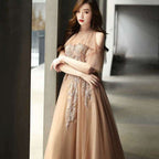 Woman in a beige evening gown with intricate detailing standing indoors.