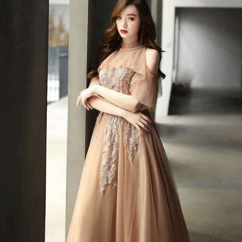 Woman in a beige evening gown with intricate detailing standing indoors.