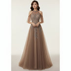 Woman in a brown evening gown with intricate detailing in a dimly lit room.